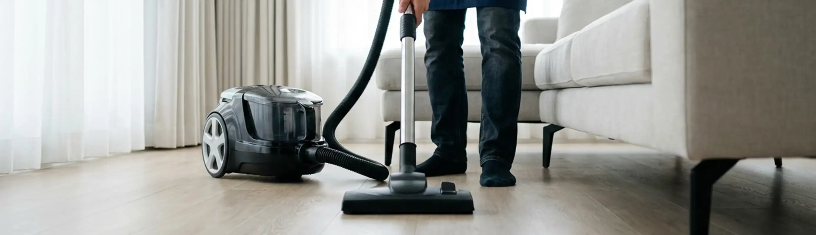 Professional house cleaner vacuuming a living room floor with a canister vacuum cleaner, Colorado Springs, CO.