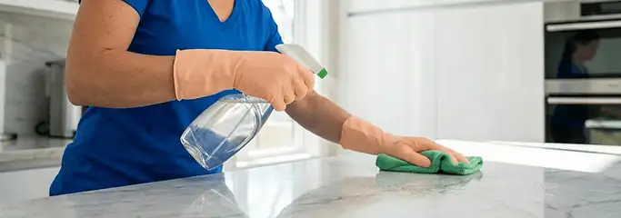 Maid service worker spraying and wiping a kitchen countertop with a microfiber cloth for sanitizing, Colorado Springs, CO.