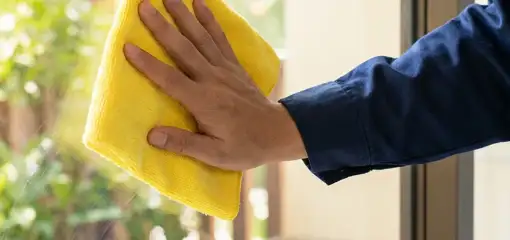 House cleaner wiping a glass window with a yellow microfiber cloth for streak-free cleaning, Colorado Springs, CO.